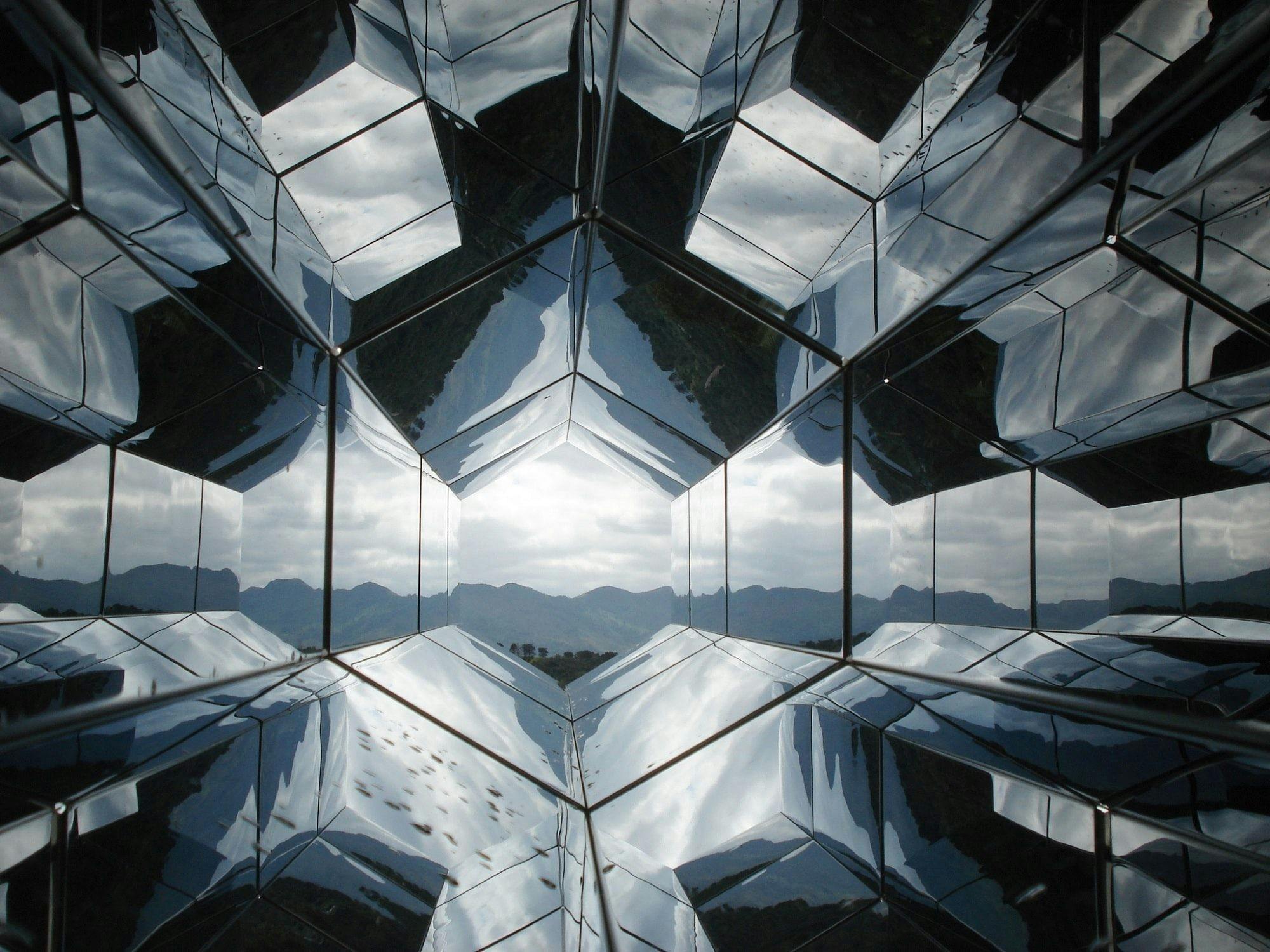 Geometric glass walls reflecting blue sky and mountains